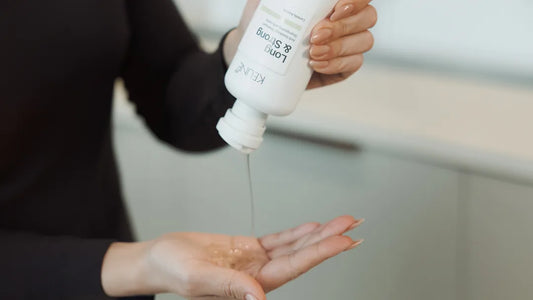 Person holding a white bottle with a pump dispenser, pouring liquid into their hand.