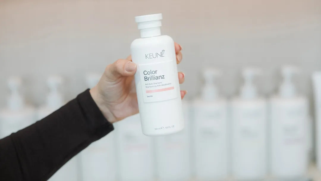 Hand holding a Keune Color Brillianz bottle against a blurred background