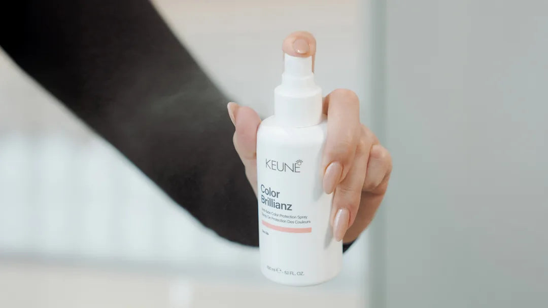 Hand holding a Keune hair care product bottle in front of a mirror.