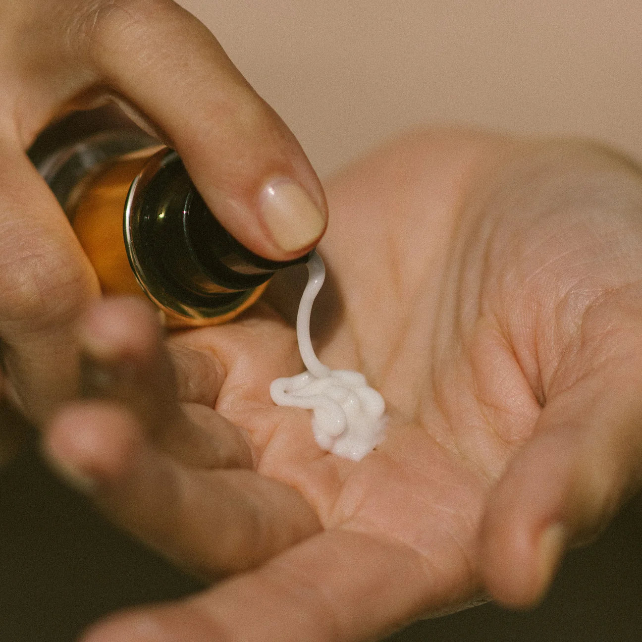 Hand holding a small bottle with a white substance being squeezed out onto another hand.