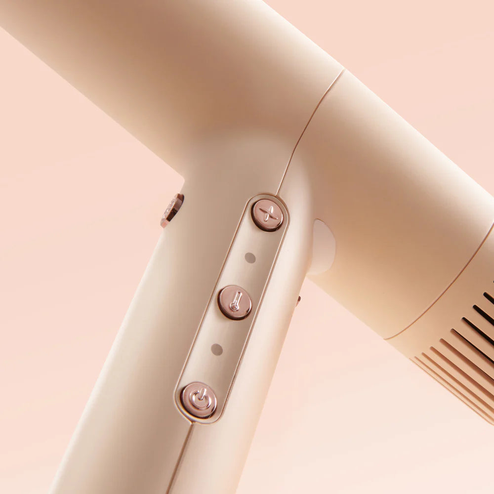 Beige hair dryer with control buttons on a light pink background