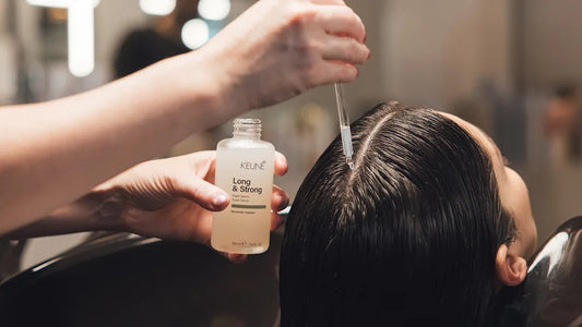 Person applying hair product to another person's hair with a bottle labeled 'Kerastase'.