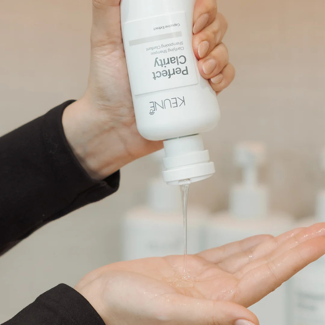 Person holding a KEUNE hair care product bottle over their palm, with a blurred background.