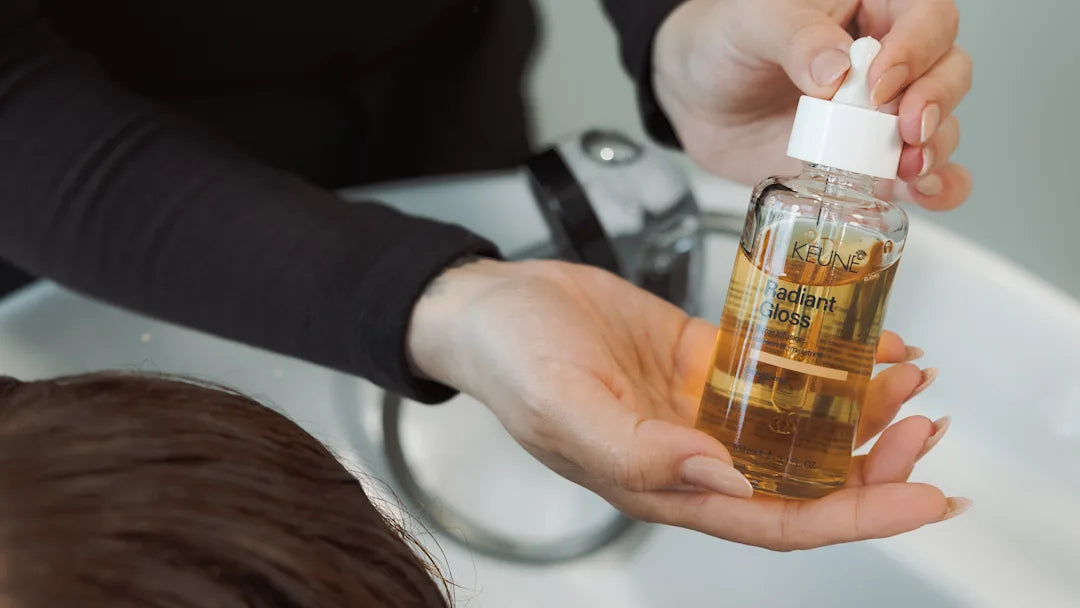 Person holding a bottle of Keune Radiant Gloss hair oil with a dropper.