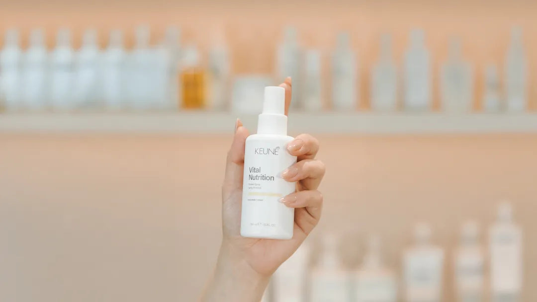 Hand holding a skincare bottle with a blurred background of more bottles.