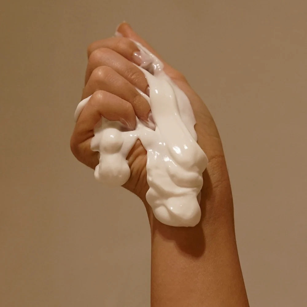 Hand holding a generous amount of white cream against a beige background