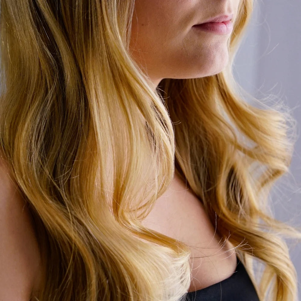 Close-up of a person with long, wavy blonde hair against a neutral background