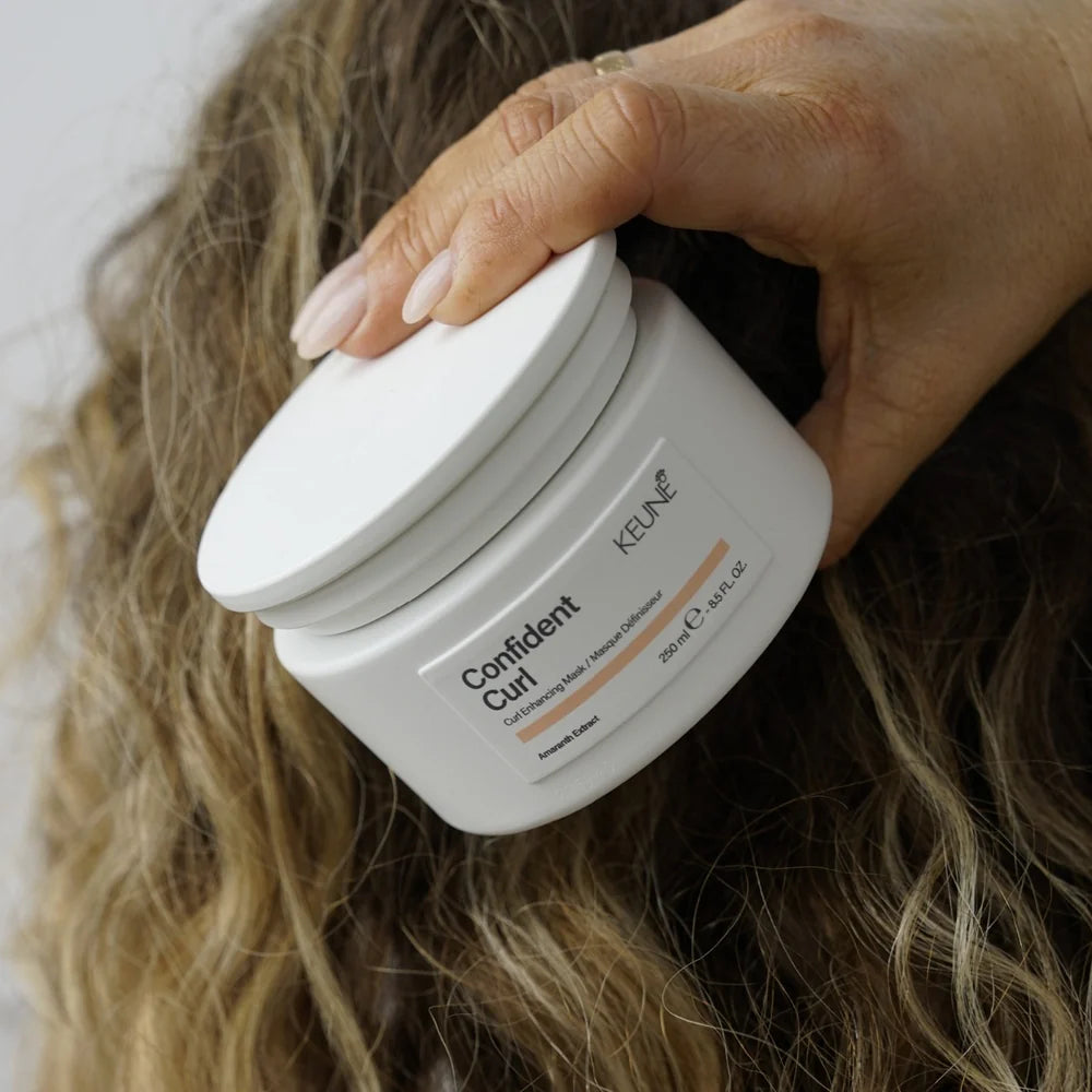 Person holding a jar of Keune Confident Curl product with hair in the background