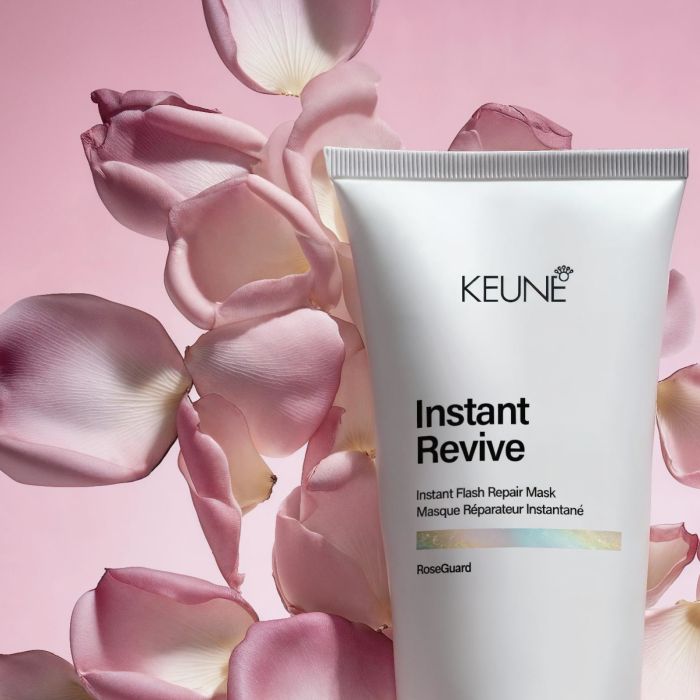 A white squeeze tube of KEUNE Instant Revive Instant Flash Repair Mask standing upright among soft pink rose petals against a pink background.